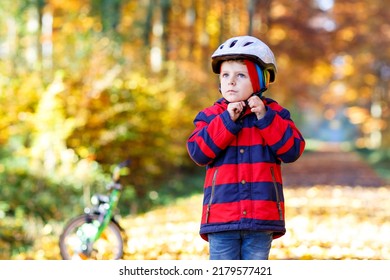 Little Kid Boy In Colorful Warm Clothes In Autumn Forest Park With A Bicycle. Active Child Putting Safe Helmet Before Cycling On Sunny Fall Day In Nature. Safety, Sports, Leisure With Kids Concept