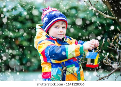 Little Kid Boy Feeding Birds In Winter. Cute Happy Preschool Child Hanging Colorful Selfmade Bird House On Tree On Frosty Cold Day. Toddler In Colorful Wam Clothes Putting Seeds In Feeder