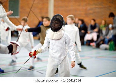 Little kid boy fencing on a fence competition. Child in white fencer uniform with mask and sabre. Active kid training with teacher and children. Healthy sports and leisure.