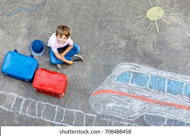 Little kid boy having fun with fast train picture drawing with colorful chalks on asphalt. Child painting with chalk and crayon and going on vacations. Schoolkid sitting on suitcase