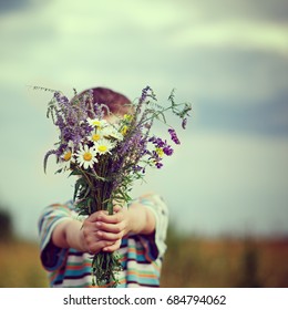 Little Kid Boy In Meadow Bouquet Of Flowers At The Countryside. Child Giving Flowers.