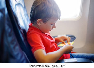 Little Kid Boy Playing Tic Tac Toe Game During Flight On Airplane. Child Sitting Inside Aircraft By A Window. Family Going On Vacation. Passenger Having Fun With Toy.