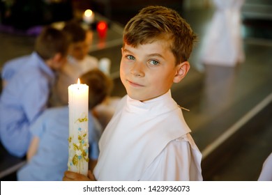 Little Kid Boy Receiving His First Holy Communion. Happy Child Holding Christening Candle. Tradition In Catholic Curch. Kid In A White Traditional Gown In A Church Near Altar.