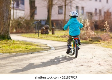 Little kid boy riding with his first green bike in the city park. Happy child in colorful clothes. Active leisure for kids outdoors.