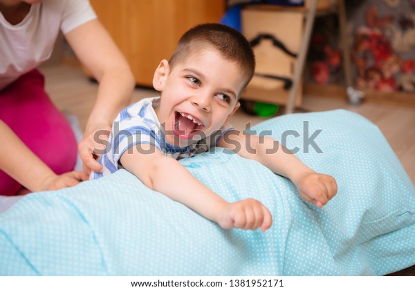 little kid with cerebral palsy has musculoskeletal\
therapy by doing exercises in body fixing. Load on hands,cheerful\
boy with disability at rehabilitation center for kids with special\
needs