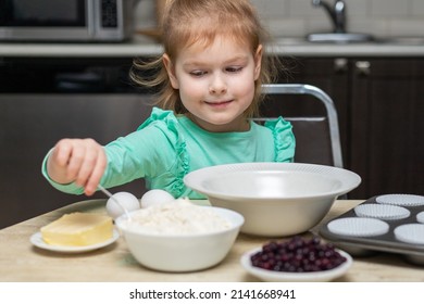 Little Kid Cooking Food. Small Child Baking Cupcakes At Home Sitting At Table With Food In Kitchen. Kid Mixing Ingredients For Muffins In Bowl.