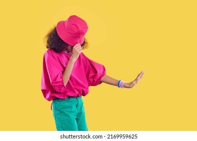 Little Kid Dancing. Child In Trendy Outfit Posing Isolated On Solid Yellow Color Fashion Studio Background. Side Profile View African American Girl In Fuschia Bucket Hat And Green Pants Doing Moonwalk