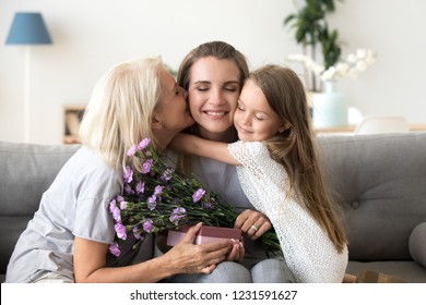 Little kid daughter and old mother kissing embracing young woman congratulating with birthday, senior grandmother and child girl presenting happy mom flowers gift box, 3 generation celebrate together - Powered by Shutterstock