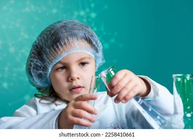 Little kid doing experiments with blue liquid. Cute child wants to become a doctor. Pretty child in white medical robe holds glass flasks with blue liquid on indigo background with hospital symbol. - Shutterstock ID 2258410661