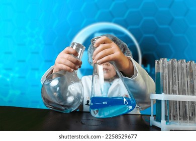 Little kid doing experiments with blue liquid. Cute child wants to become a doctor. Pretty child in white medical robe holds glass flasks with blue liquid on indigo background with hospital symbol. - Shutterstock ID 2258529677