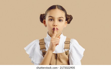 Little kid doing silencing gesture. Child hiding important secret. Beautiful girl with cute hair buns looking at camera, holding her finger on lips and asking you to not share top secret information - Shutterstock ID 2173322905