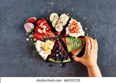 Little kid eating sliced, juicy watermelon pizza with banana, avocado, blueberries, strawberries, tomato, citrus and cottage cheese