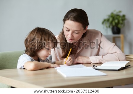 Little kid excitedly writing and sketching in notebook, with mother's encouragement and assistance. Mom and son, teaching and interests go hand in hand. Children's abilities inventiveness developing.