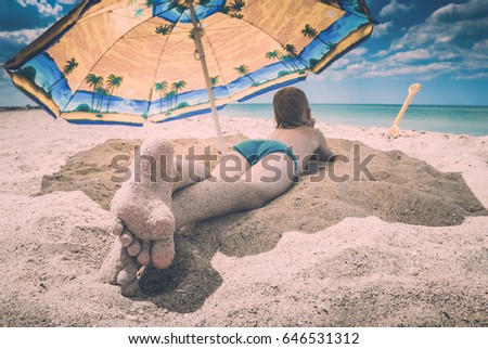 Little kid with feet in send lying on a sandy beach under umbrella. Instagram stylization.
