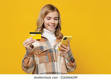 Little kid girl 13-14 years in checkered shirt using mobile cell phone hold credit bank card do online shopping order delivery booking tour isolated on plain yellow background People lifestyle concept - Shutterstock ID 2163466249