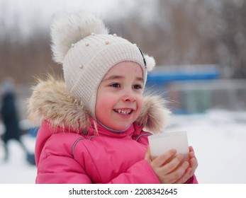 Little Kid Girl With A Cup Of Warm Cocoa Outdoors For Christmas. Child On A Walk In The City Park. Family Winter Vacation. An Alternative To Computer Games. A Girl In A Pink Jacket Drinks Hot Tea 