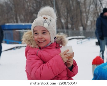 Little Kid Girl With A Cup Of Warm Cocoa Outdoors For Christmas. Child On A Walk In The City Park. Family Winter Vacation. An Alternative To Computer Games. A Girl In A Pink Jacket Drinks Hot Tea 