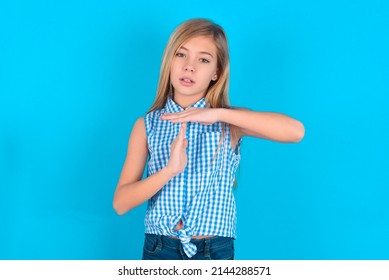 little kid girl with glasses wearing plaid shirt over blue background feels tired and bored, making a timeout gesture, needs to stop because of work stress, time concept.