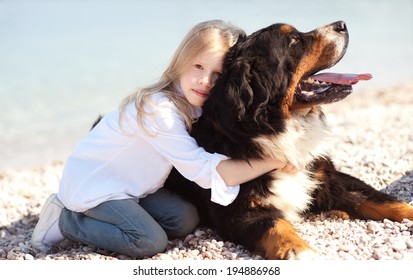 Little Kid Girl Holding Bernese Mountain Dog At Beach