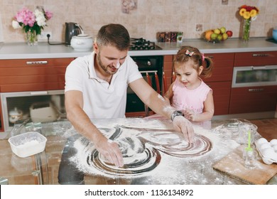 Little Kid Girl Plays With Man Draws Heart On Scattered Flour In Kitchen At Table. Happy Family Dad, Child Daughter Cooking Food Cookies In Weekend Morning. Father's Day Holiday. Parenthood Childhood