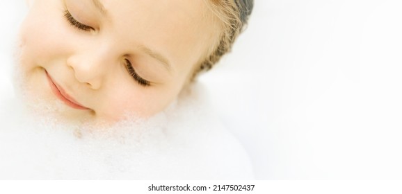 Little Kid Girl Taking Bath With White Foam Soap Bubbles With Copy Space For Text. Personal Hygiene Child And Skincare Concept. Selective Focus.