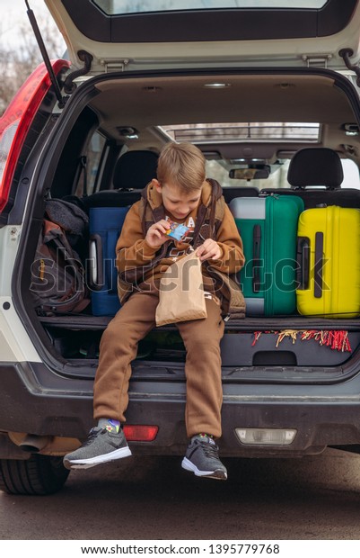 little kid looking into paper bag with candies\
sitting in car trunk full of\
bags.