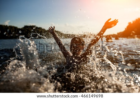 little kid play in water and making splash; child swim in lake or river and have fun with drops;