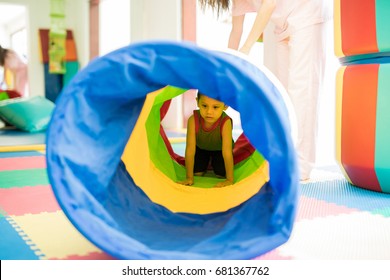 Little kid playing and crawling through a tunnel in an obstacle course at a children physical therapy center