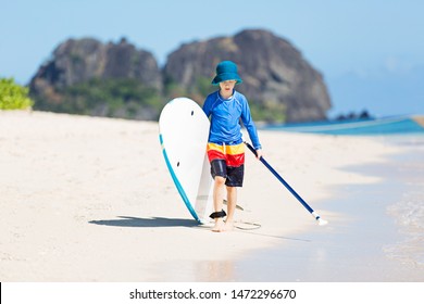 Little Kid In Rashguard Holding Stand Up Paddleboard And Walking At Beautiful White Sand Beach At Fiji Island, Active Family Vacation Concept