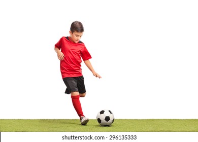 Little Kid In Red Football Jersey Kicking A Football On A Grass Surface Isolated On White Background
