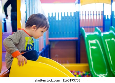 Little kid riding from childrens slides in game center. Happy little kid, children riding up, down on slide, in game center, amusement park of the children's room