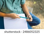 A little kid is sharpening his pencil with a sharpener in the park, back to school concept