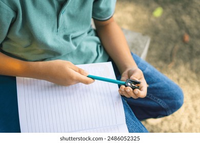 A little kid is sharpening his pencil with a sharpener in the park, back to school concept