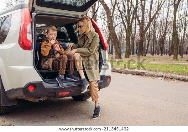 little kid sitting\
with mother in car trunk full of luggage eating chocolate candies.\
car travel concept