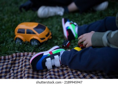 Little Kid Is Sitting On The Grass And Playing With His Toys. Childhood, Baby And Playing Toys Concept. No People Face In Photo. Unrecognizable Person. The Focus Is On His Hand.