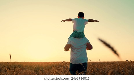 Little kid superhero imagines soaring through sky at sunset. Loving father runs with playful son on shoulders through wheat field. Happy child daydreams about pilot gliding in golden glow of sunset - Powered by Shutterstock