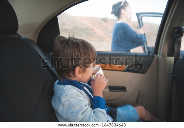little kid in sweater drinking cup of tea\
inside car with mother woman calling\
outside