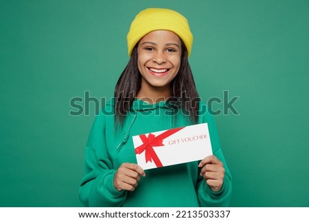 Little kid teen girl of African American ethnicity 13-14 years old wear casual hoody hat hold gift certificate coupon voucher card for store isolated on plain dark green background Childhood concept