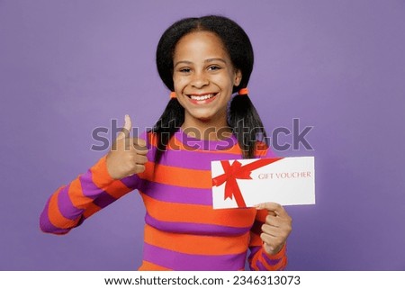 Little kid teen girl of African American ethnicity 15 years old wear orange sweatshirt hold store gift certificate coupon voucher show thumb up isolated on plain purple background. Childhood concept
