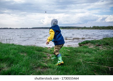 Little Kid Throwing Rocks In Lake. Rubber Boots