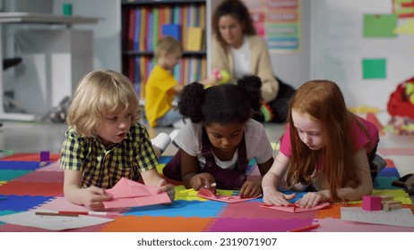 Little kids learn to folding paper origami lying on floor in kindergarten. Diverse preschool children doing craft at nursery school playroom - Shutterstock ID 2319071907