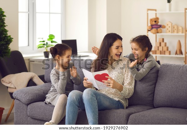 Little kids making surprise for mommy. Excited\
young woman thanking her children for handmade card on Happy\
Mother\'s Day. Cute twin daughters clapping hands and wishing their\
mom love and happiness