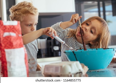 Little Kids Mixing Batter In A Bowl For Baking, With Girl Licking A Spoon. Children Baking In The Kitchen.