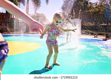 Little Kids Are Playing Outside In The Water Fountains At An Outdoor Splash Pad Park On A Summer Day.