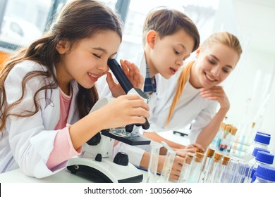 Little kids with teacher in school laboratory looking in microscope
