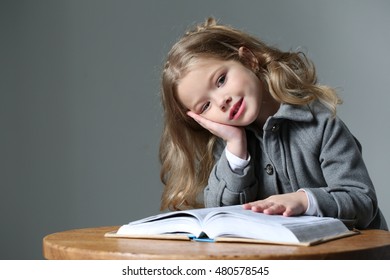 Little lady sitting at the table with a book. Close up. Gray background