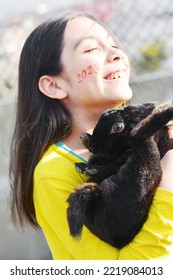 Little latin girl holding a black rabbit. 2023 written on the cheek. Focus on the rabbit. - Shutterstock ID 2219084013