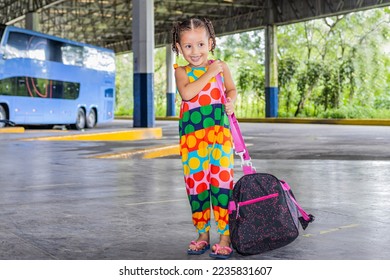 Little latina and brazilian girl with a big bag waiting for a bus at the bus station - Powered by Shutterstock