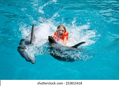 Little Laughing Girl Swimming with the Dolphins in the Swimming Pool in the Bright Sunny Day