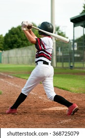 Little league baseball player at the plate, swinging the baseball bat from behind.